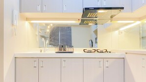 A modern kitchen with white cabinetry, a stainless steel range hood, and a large mirror above the countertop. - Good Choice And Homey 2Br Signature Park Grande Apartment (Jakarta)
