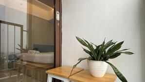 Quarto de hotel com uma cama, um banquinho de madeira e uma planta em vaso.