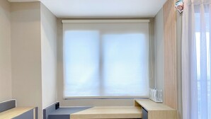 Quarto moderno com uma janela grande, banco embutido e escrivaninha de madeira.