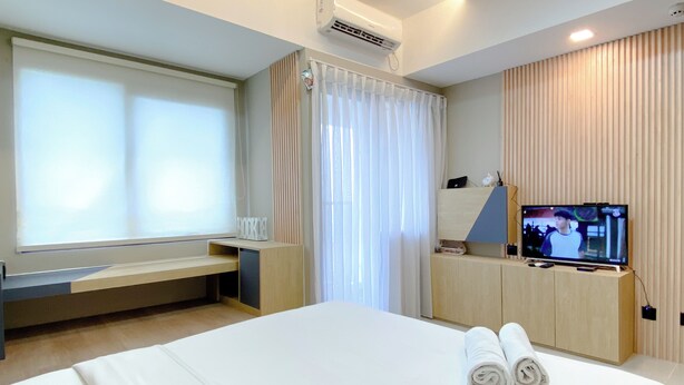 Quarto de hotel com cama, televisão, escrivaninha e janela com cortinas.
