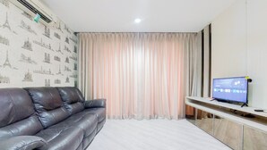 A living room with a black leather sofa, a television on a stand, and a curtain with a cityscape wallpaper.