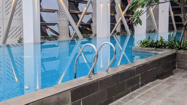 A modern indoor pool with clear glass walls, metal handrails, and a geometric architectural design.