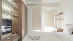 A hotel room with a bed, a TV on a wooden shelf, an air conditioner, and a door leading to another room. - Best Deal And Homey Studio Apartment Amazana Serpong (South Tangerang)