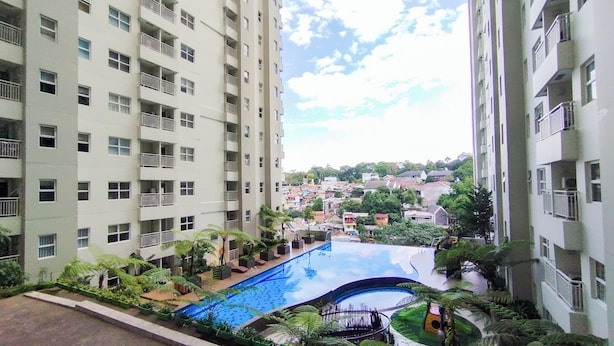 A high-rise building with multiple balconies and a swimming pool surrounded by greenery. - Simple 1Br Apartment Parahyangan Residence (Bandung)