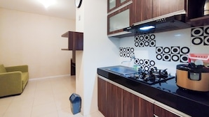 A compact kitchen with a gas stove, a built-in oven, and a microwave. There is a clock on the wall and a trash bin near the entrance. - Simple 1Br Apartment Parahyangan Residence (Bandung)