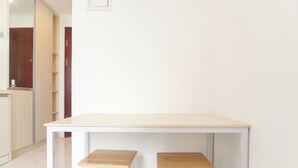 Ein weißer Tisch mit zwei hölzernen Hockern in einem Raum, im Hintergrund eine weiße Wand und eine Holztür.