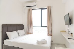 Quarto de hotel com cama, cortinas, ar condicionado, televisão e mesa de trabalho com controle remoto.