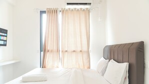 A neatly made bed with white linens and pillows, a headboard, and a window with sheer curtains. - Furnished And Cozy Studio Sky House Alam Sutera Apartment (Tangerang)