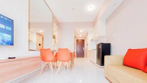 A modern living room with a sofa, a TV mounted on the wall, and a dining area with chairs and a table.