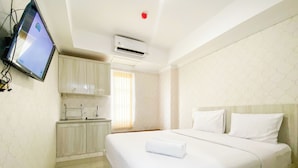 A hotel room with a bed, a TV mounted on the wall, a kitchenette, and an air conditioning unit. - Cozy And Minimalist Studio Paltrow City Apartment (Semarang)