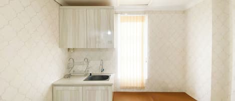 A small, compact room with a kitchenette, a single bed, and a window with blinds.