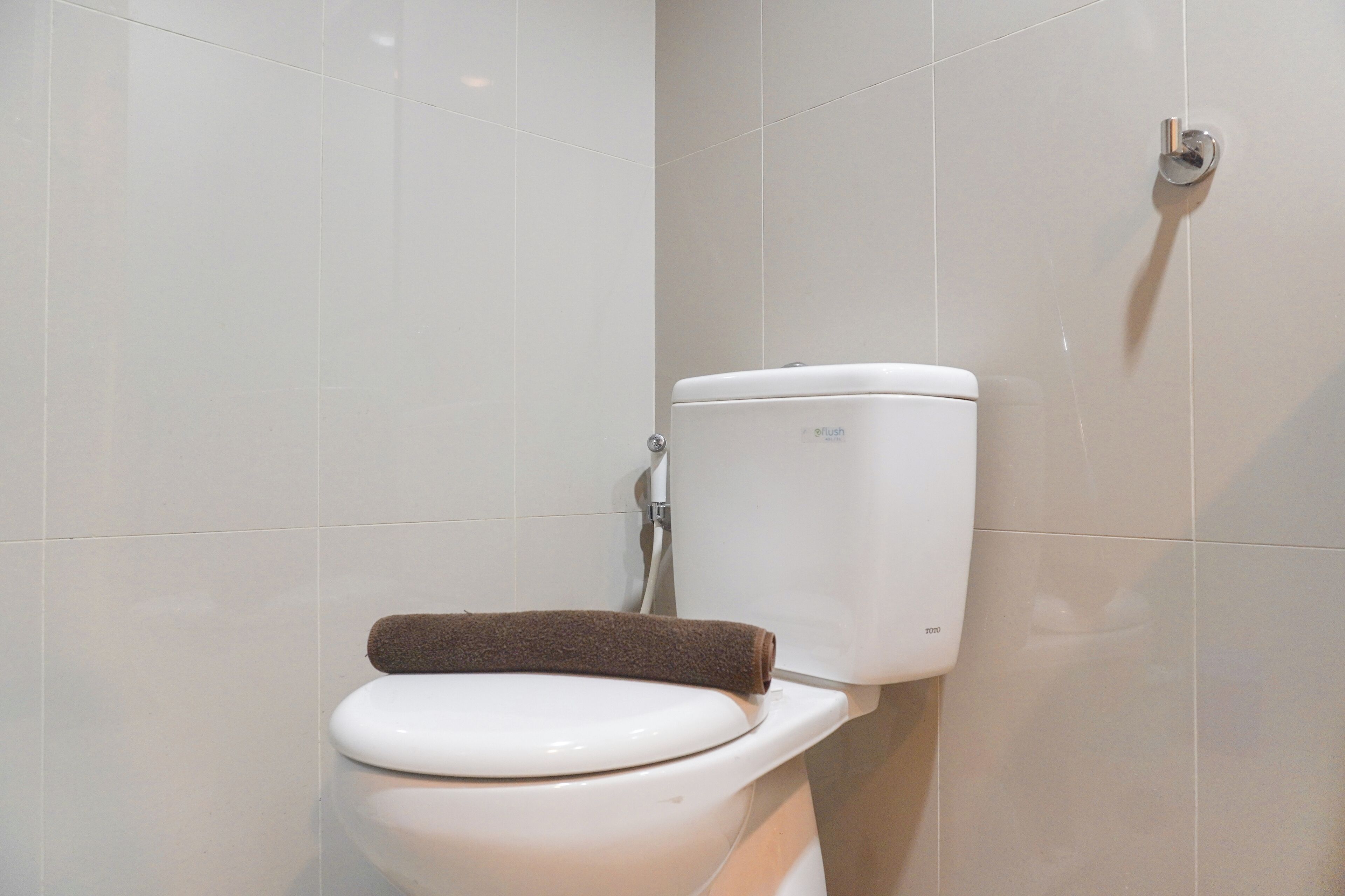 Et toilet med et brunt håndklæde på sædet i et badeværelse med hvide flisevægge.