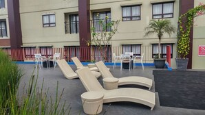Terraza en la azotea con sillones y mesas, rodeada por un cerco bajo y plantas en macetas.