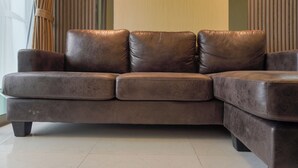 Een bruine leren hoekbank met chaise longue, geplaatst in een kamer met een groot raam en gordijnen.