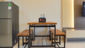 Een compacte kitchenette met een koelkast, een houten tafel met bankjes en een waterdispenser op het aanrecht.