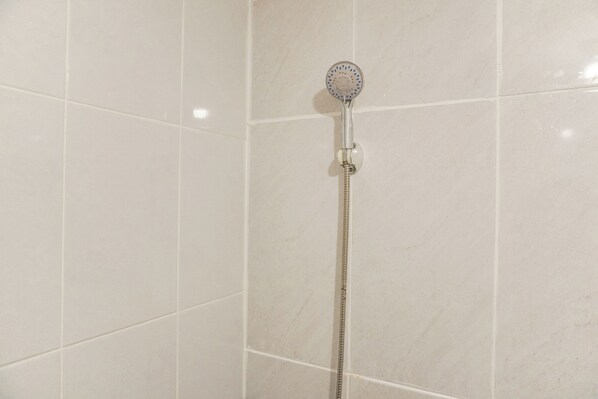 A shower with a handheld showerhead mounted on a wall, a flexible hose, and a control knob.