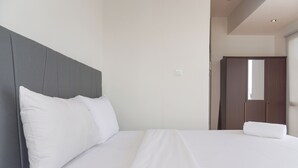 Una cama bien hecha con sábanas y almohadas blancas, un cabecero gris y un armario de madera al fondo.
