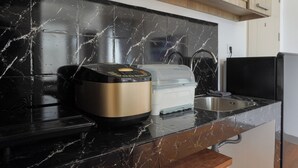 Una cocina con encimera de mármol negro, una cocedora de arroz, un procesador de alimentos y un lavamanos.