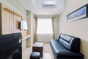 Una sala de estar moderna con un sofá de cuero negro, un televisor de pantalla plana montado en un panel de madera, una mesita y una ventana con cortinas.