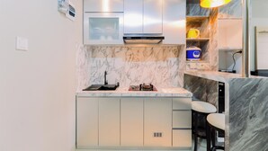 A modern kitchen with a marble countertop, stainless steel appliances, and a built-in bar area with stools. - Homey And Minimalist 1Br Royal Sentul Park Apartment (Bogor)