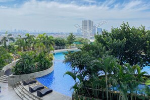 A rooftop pool with steps leading down to lounge areas, surrounded by lush greenery. - Good Choice And Best Location Studio West Vista Apartment (Jakarta)