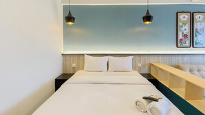 Hotellihuone, jossa on siististi pedattu sänky, kaksi yöpöytävalaisinta, puinen yöpöytä ja puinen penkki.
