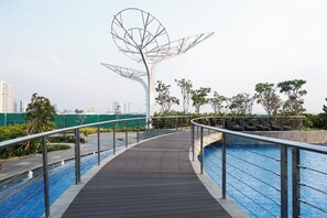 A wooden deck with a metal railing, a pool, and a decorative metal structure. - Good Choice And Best Location Studio West Vista Apartment (Jakarta)