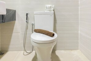 A white toilet with a towel on top, a handheld showerhead, and a toilet paper holder. - Good Choice And Best Location Studio West Vista Apartment (Jakarta)