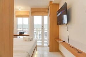 Habitación de hotel con cama, televisión instalada en la pared, una mesita con un control remoto y ventana con vista al exterior.