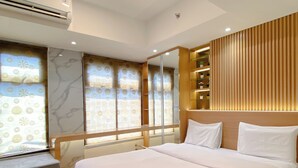 A modern hotel room with a large bed, a built-in wardrobe, a vanity with a mirror, and a window with patterned curtains.