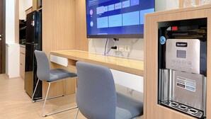 A modern kitchen with a flat-screen TV displaying a Netflix interface, a water dispenser, and a seating area with a chair and a small table.
