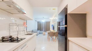 A modern kitchen with a built-in stove, a dining area with a table and chairs, and a living area with a sofa and a TV. - Comfy 3Br Sky House Bsd Apartment (Pagedangan)