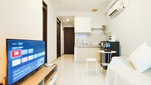 A modern hotel room with a flat-screen TV, a sofa, a small dining table, and a kitchenette in the background. - Modern 2Br At Mekarwangi Square Cibaduyut Apartment (Bandung)