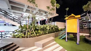 A modern building with a staircase leading to an upper level, surrounded by greenery and a small yellow kiosk.