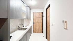 A narrow hallway with a kitchen area on one side, featuring cabinets, a sink, and a wooden door.