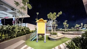 A nighttime outdoor area with a yellow play structure, green artificial turf, and palm trees.