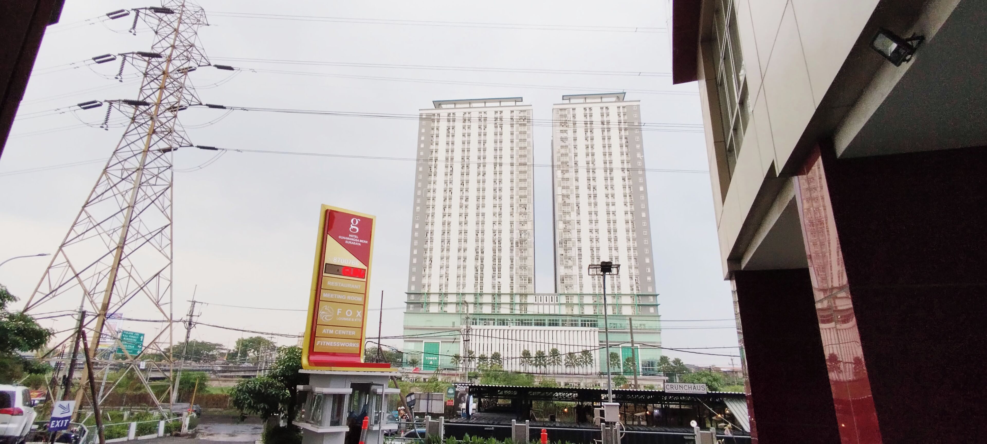 Un edificio de gran altura con varios pisos, un cartel llamativo que anuncia diversos servicios, y una torre de servicios en primer plano.