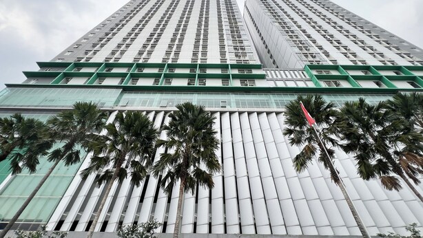 A high-rise building with a modern architectural design, featuring a grid of windows and a prominent green structural element. - Simple And Comfortable Living Studio At Bale Hinggil Apartment (Surabaya)