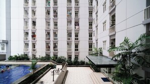 A high-rise residential building with multiple balconies, a swimming pool, and surrounding greenery. - Simple And Comfortable Living Studio At Bale Hinggil Apartment (Surabaya)