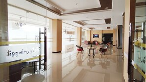 A modern hotel lobby with a glass partition, a reception desk, and a seating area with chairs and tables. - Simple And Comfortable Living Studio At Bale Hinggil Apartment (Surabaya)