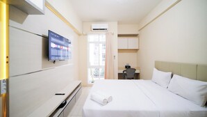 A hotel room with a bed, a desk, a chair, a TV mounted on the wall, and an air conditioning unit. - Simple And Comfortable Living Studio At Bale Hinggil Apartment (Surabaya)