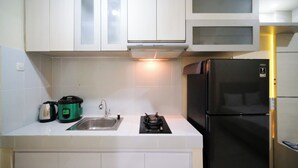 A kitchen with white cabinets, a black refrigerator, a sink, and a gas stove. - Simple And Comfortable Living Studio At Bale Hinggil Apartment (Surabaya)