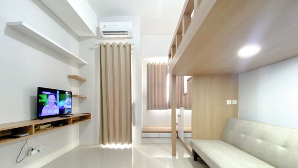 A modern hotel room with a flat-screen TV, a sofa, a ceiling fan, and a window with curtains. - Restful And Well Designed Studio Transpark Juanda Bekasi Timur Apartment (Bekasi)