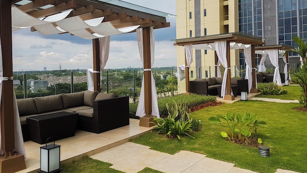 A rooftop patio with outdoor seating, a glass pergola, and a view of a cityscape. - Modern Look And Cozy 1Br Branz Bsd City Apartment (Pagedangan)