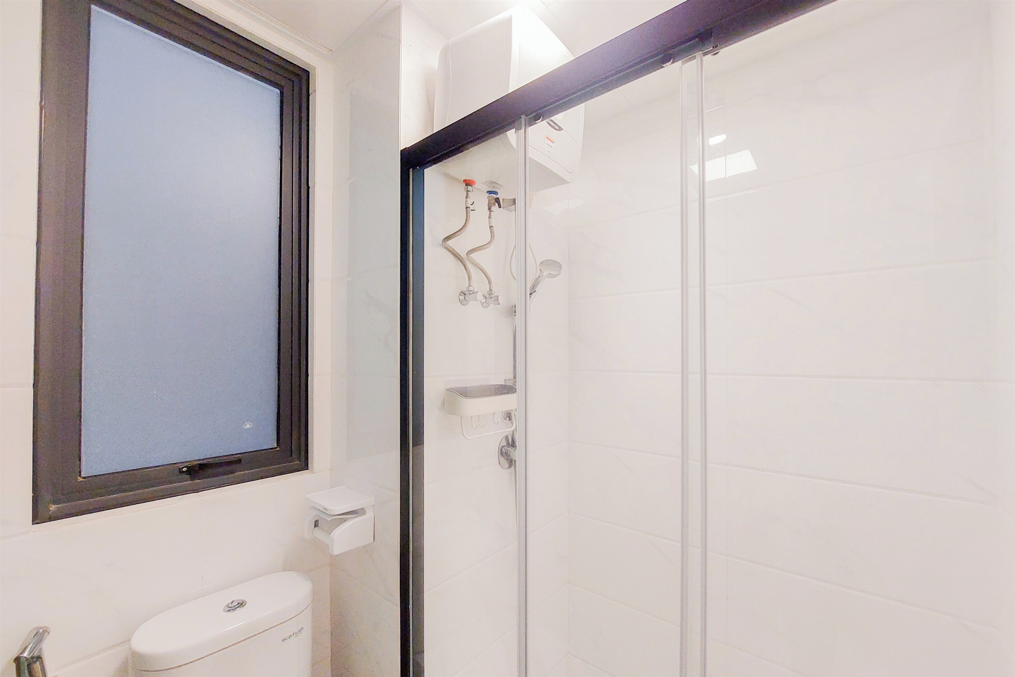 Un baño con inodoro, ducha con mampara de vidrio y ventana sobre el inodoro.