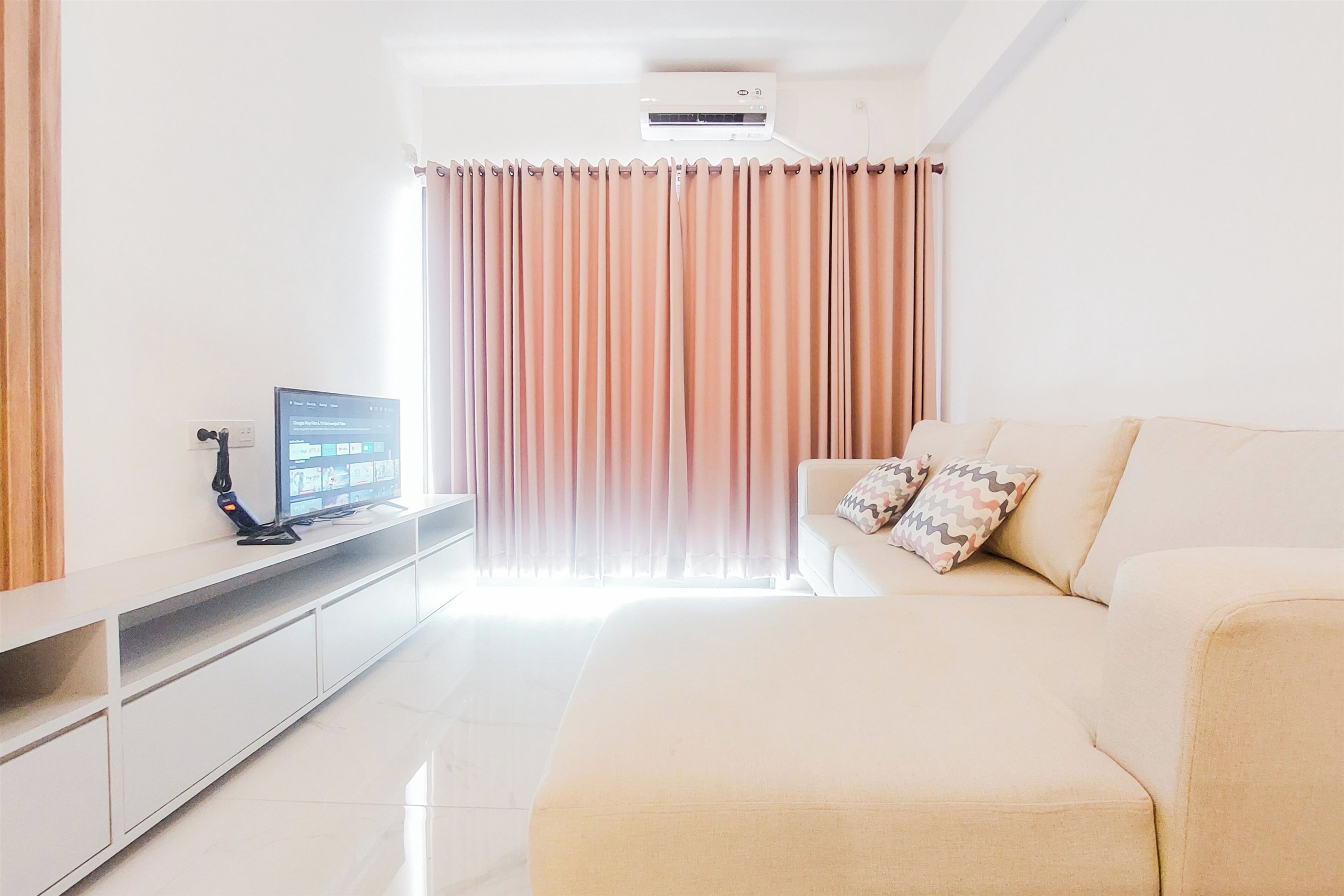 Una sala de estar moderna con un sofá, un televisor sobre un mueble bajo y un ventanal con cortinas.