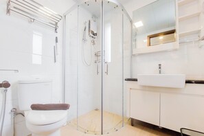 A modern bathroom with a glass-enclosed shower, a white toilet, and a sink with a mirror above it. - Spacious And Homey Living 3Br At Sky House Bsd Apartment (Pagedangan)