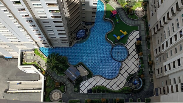 An aerial view of a modern building with a large central pool surrounded by a landscaped area with palm trees and a circular fountain. - Best Deal And Restful 2Br Marina Ancol Apartment (Jakarta)