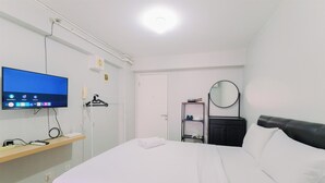 A hotel room with a bed, a TV on a stand, a mirror, and a shelf with toiletries.
