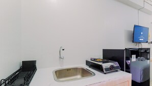 A modern kitchen with a stainless steel sink, a black dish rack, a portable stove, and a flat-screen TV mounted on the wall.
